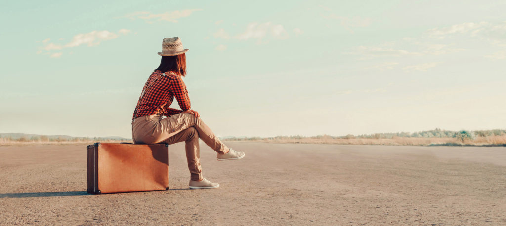 Traveler woman sits on retro suitcase and looks away on road